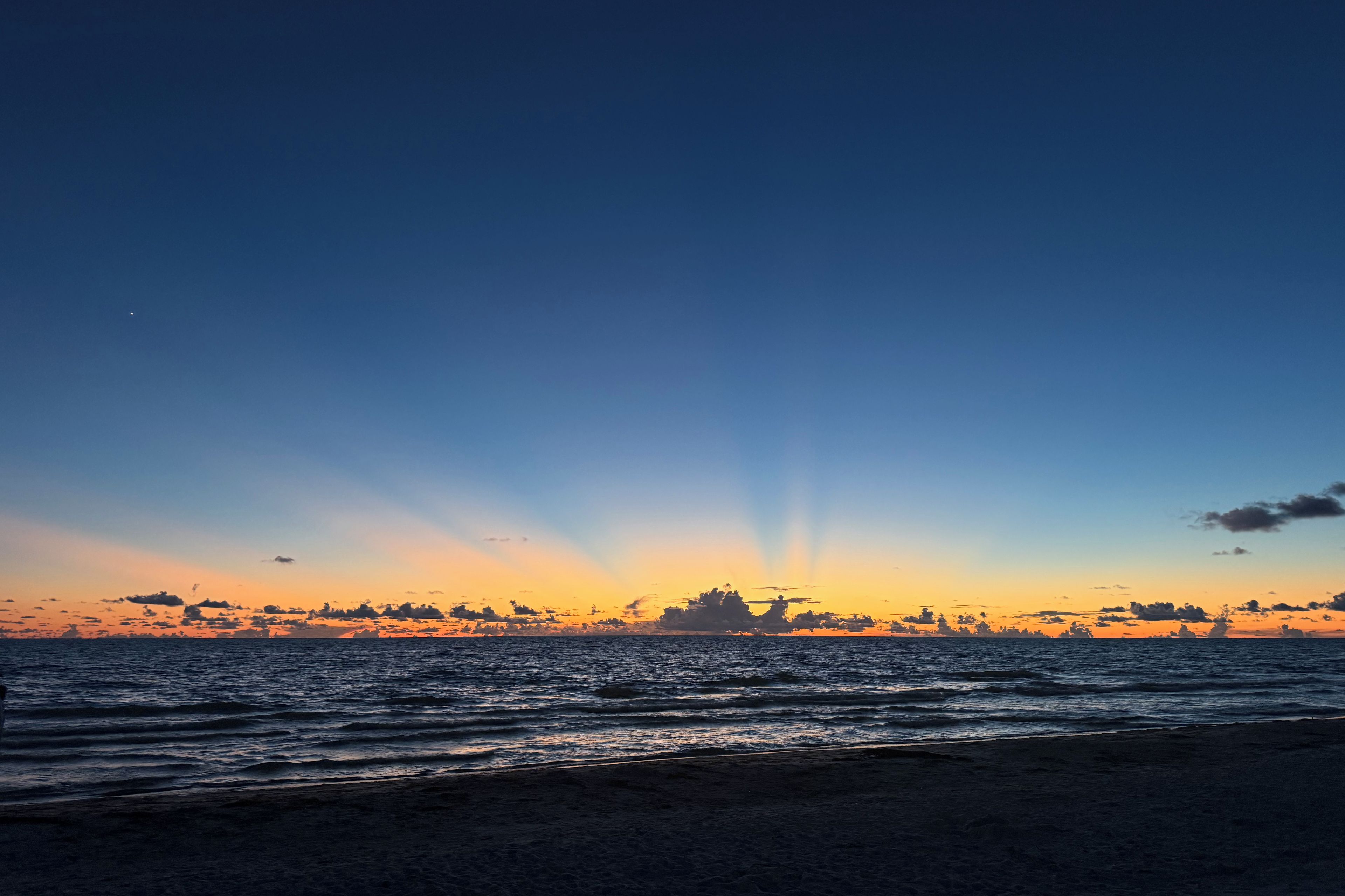 A beach at sunset with waves and a clear sky.