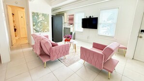 Un salón moderno con muebles tapizados en rosa, un televisor de pantalla plana y una ventana con persianas.