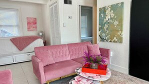 Un sofá rosa, una mesita redonda con mantel floral y un cuadro de flores en la pared.