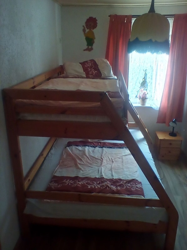 Ein Zimmer mit zwei Etagenbetten, einem kleinen Nachttisch mit Lampe und einem Fenster mit Vorhängen.