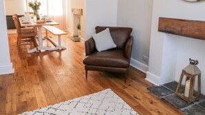 Un salon chaleureux avec un fauteuil en cuir marron, une table à manger dressée pour quatre personnes et une cheminée dotée d’une manteau en bois.