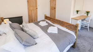 Une chambre à coucher avec un lit en bois, du linge de lit blanc, un bureau avec une chaise et deux portes en bois.