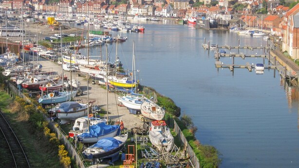 Un port de plaisance où sont amarrés de nombreux bateaux, un bâtiment historique en arrière-plan et un quartier résidentiel avec des maisons aux toits rouges.