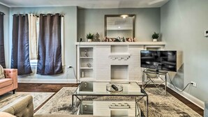 Un salon moderne avec une table basse en verre, un téléviseur à écran plat posé sur un meuble, une cheminée et un canapé.