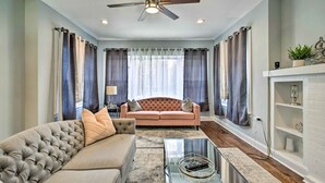 Un salon avec un canapé beige, une table basse en verre, un ventilateur de plafond et une cheminée.