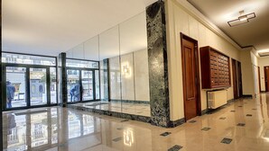 Um corredor espaçoso com pisos refletivos, amplas janelas e um pilar de mármore.