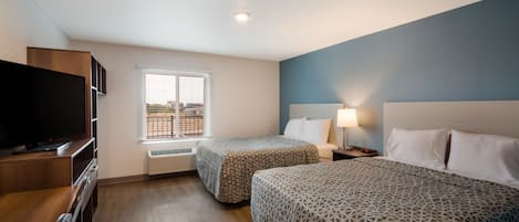 Habitación de hotel con dos camas, televisión, escritorio y ventana con vista a edificios.