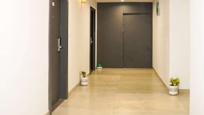 A hallway with a dark door at the end, two potted plants, and a light fixture on the wall. - Comfort Inn Udaipur (Udaipur)