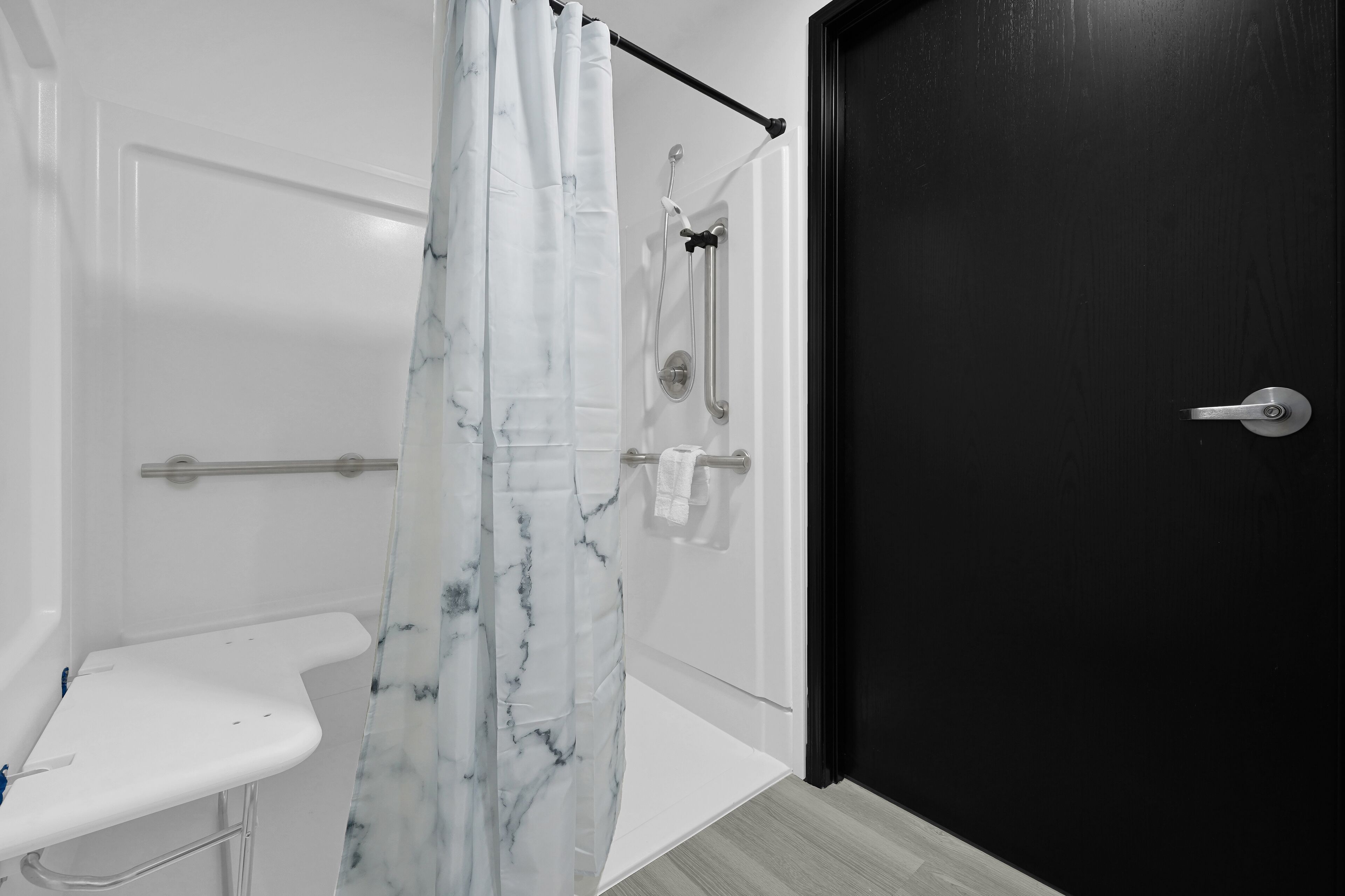 Un baño con un lavamanos blanco, una ducha con cortina de mármol y una puerta negra.