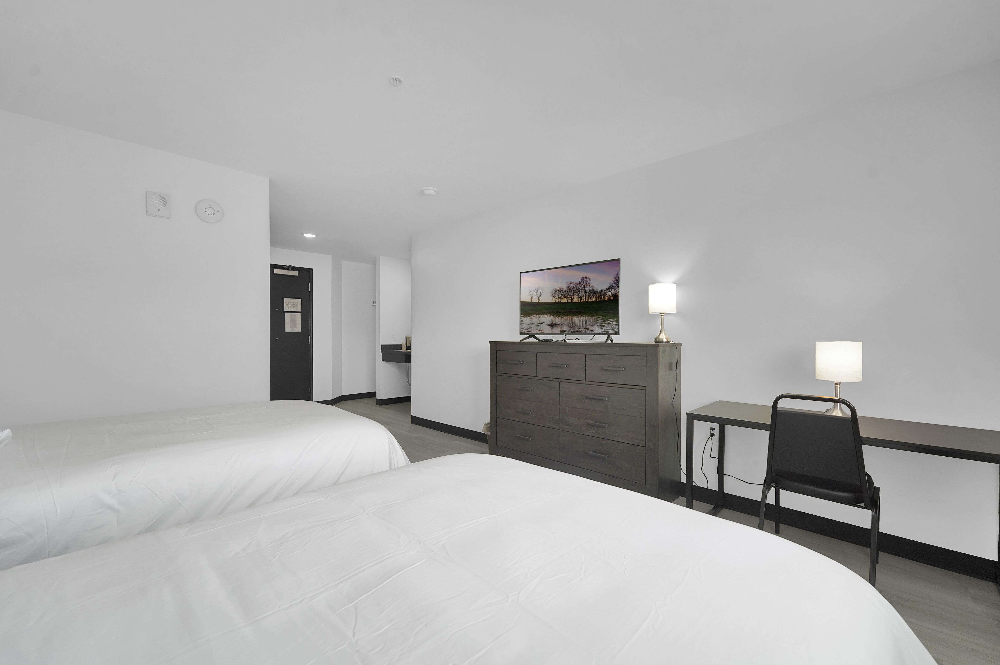 A hotel room with two beds, a desk with a chair, a dresser, and a painting on the wall.