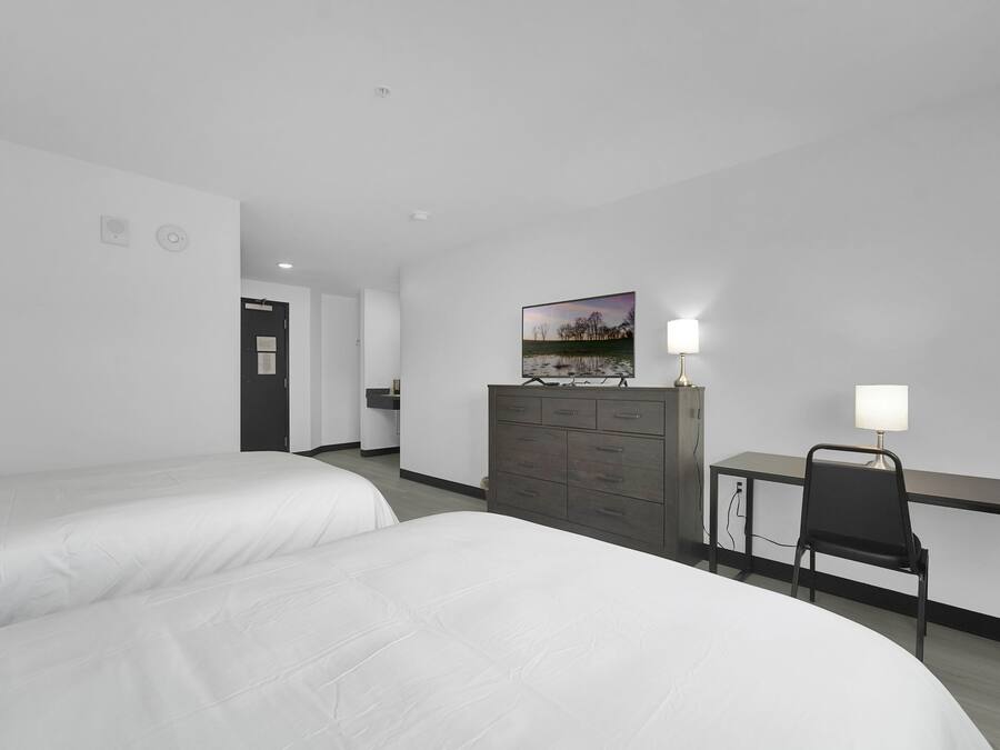 A hotel room with two beds, a desk with a chair, a dresser, and a painting on the wall.