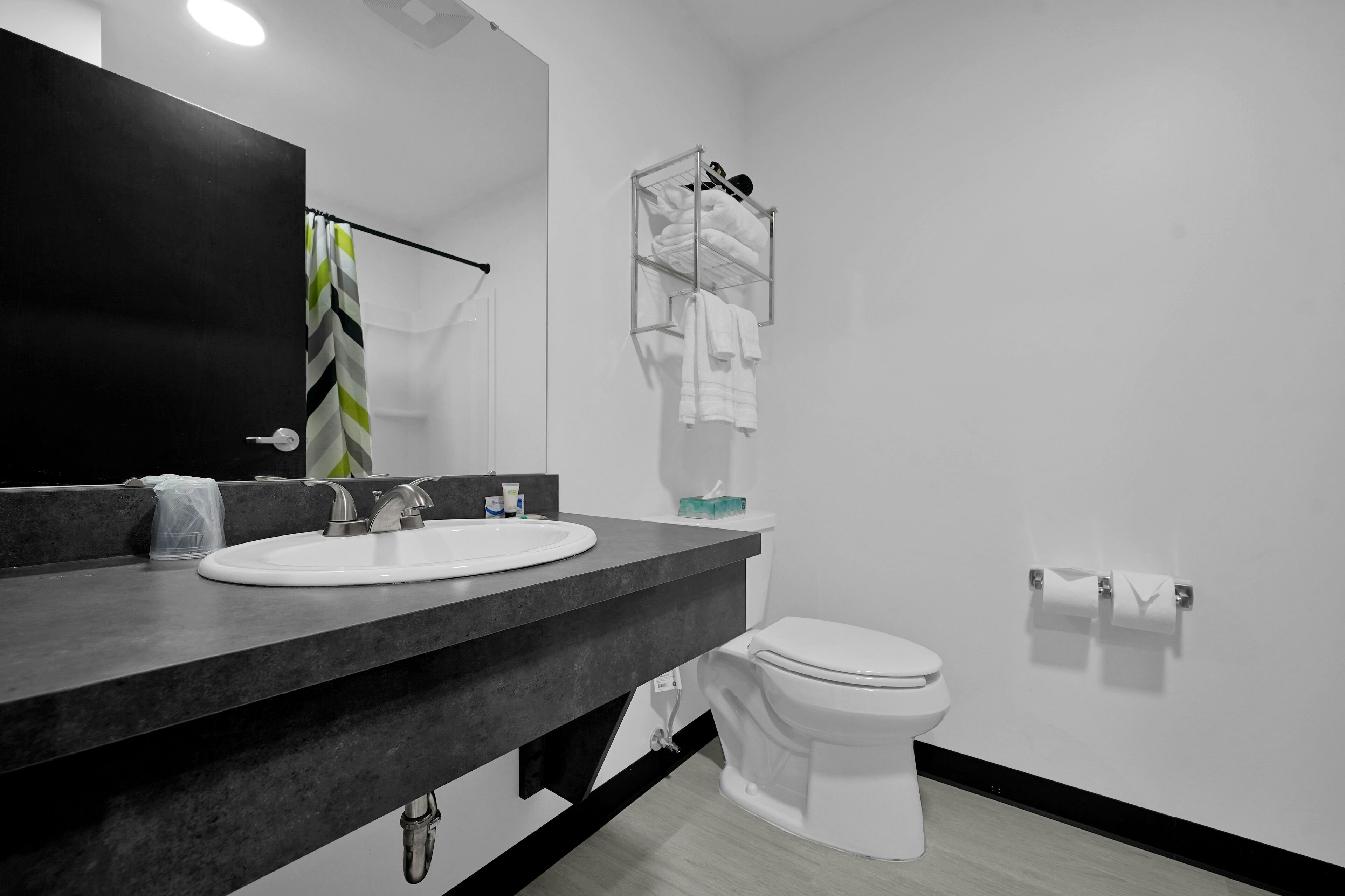Un baño moderno con encimera negra, lavamanos blanco y un inodoro.