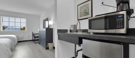 A modern hotel room with a kitchenette, a bed, a desk, and a window with a view of the outside.