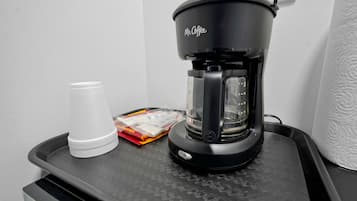 Una cafetera Mr. Coffee sobre una bandeja con una taza blanca y sobres de crema.