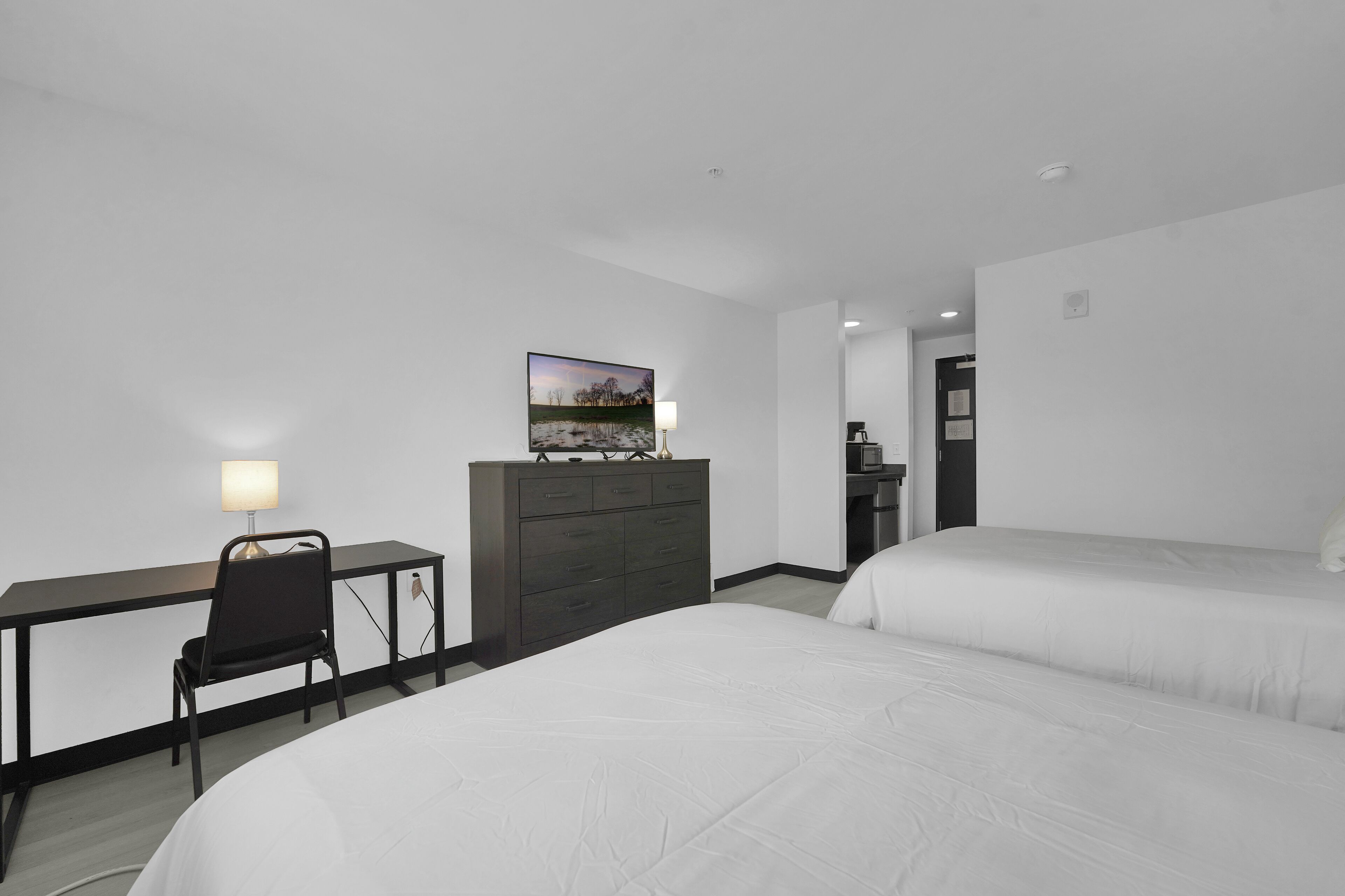 A hotel room with a desk, chair, two beds, a dresser, and a painting on the wall.