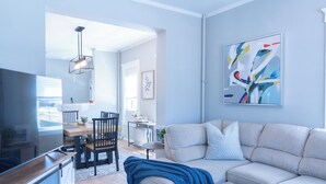 Un salon moderne comprenant un canapé, un téléviseur, une table à manger, des chaises et des œuvres d’art.