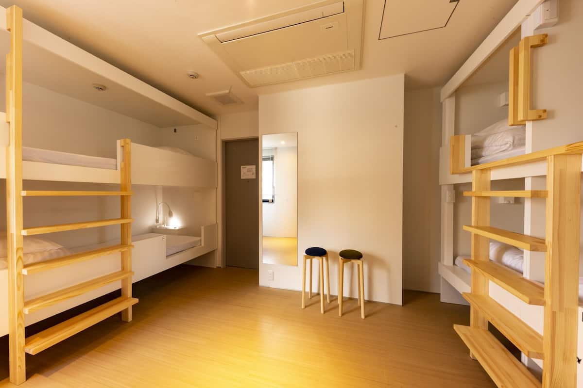 Quarto em dormitório com beliches, um banquinho pequeno e um espelho.