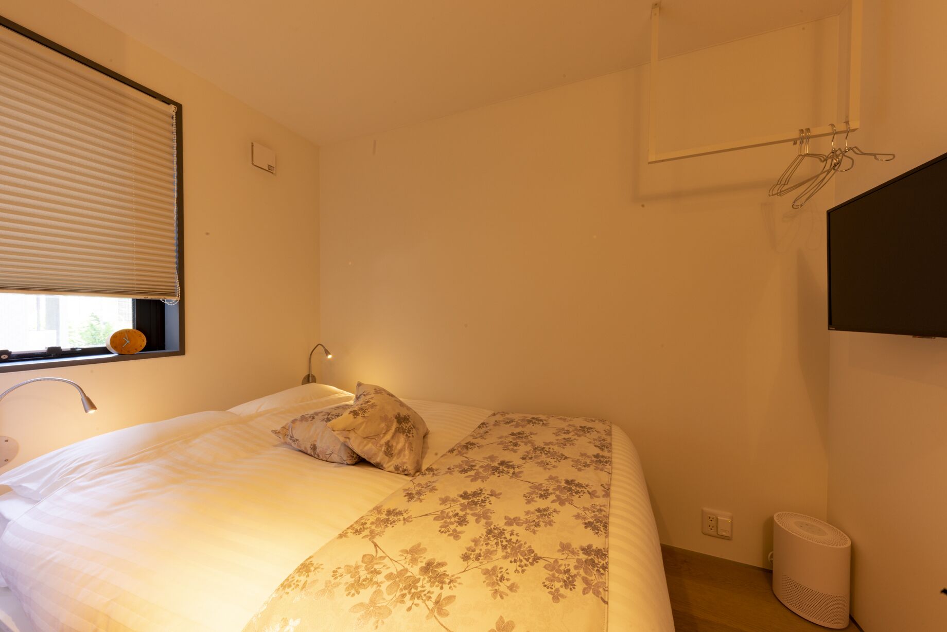 Une chambre à coucher avec un lit, une fenêtre avec des stores, une lampe fixée au mur et une prise de courant.