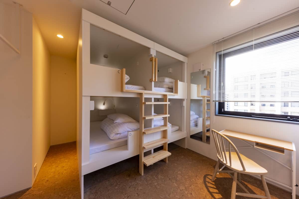 Quarto pequeno com beliches, uma escrivaninha e uma cadeira.