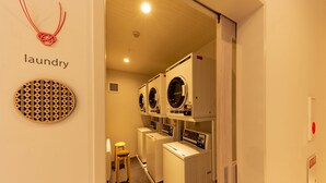 Ein Waschraum mit mehreren Waschmaschinen und Trocknern, einem Hocker und einem an der Wand befestigten, runden Schild mit dem Wort 'laundry'.