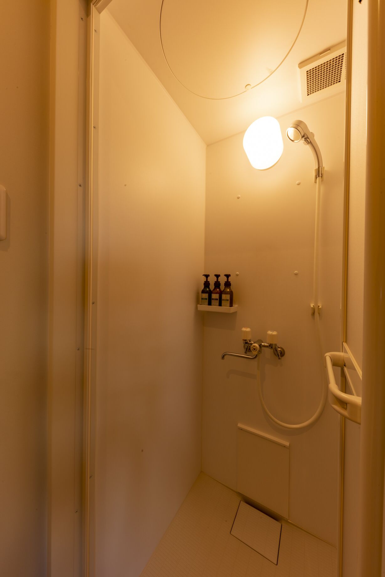 Pieni, hyvin valaistu kylpyhuone, jossa on suihku, wc ja hylly, jossa on hygieniatuotteita.