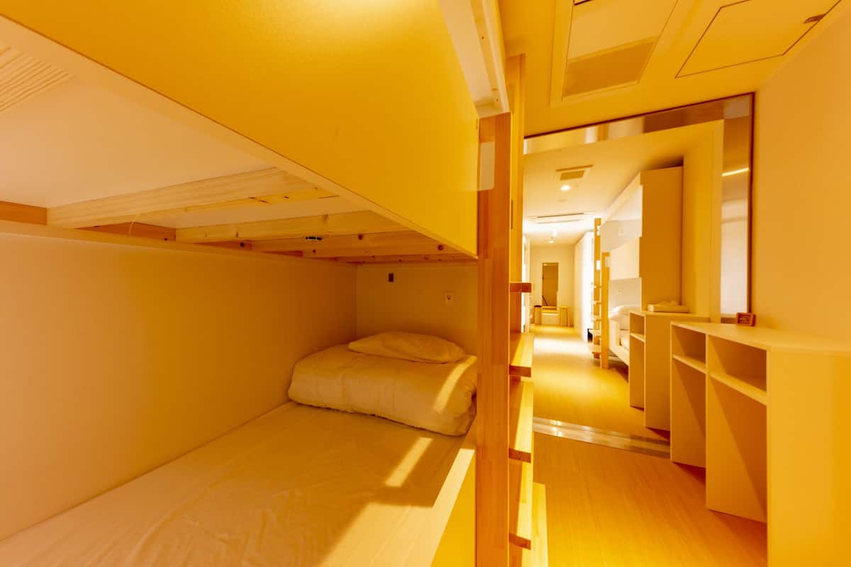 Quarto pequeno com beliches, uma escrivaninha e um espelho.