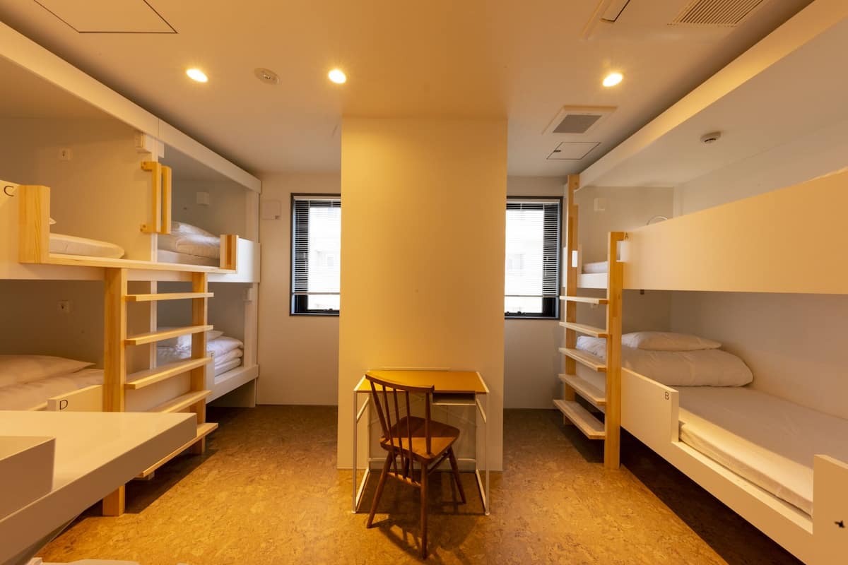 Quarto em dormitório com beliches, escrivaninha e cadeira.