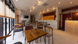 Ein modernes Café mit Holztischen und -stühlen, einem an der Wand befestigten Fernseher und einer Ziegelwand mit Regalen.