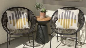 Two black wicker chairs with white cushions featuring a grid pattern, a small potted plant on a wooden table, and a concrete floor. - Newly built home minutes from Texas A&M campus (College Station)
