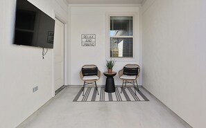 Un pasillo estrecho con dos sillones de mimbre, una mesita y una planta en maceta. Un cartel en la pared dice "RELAX AND LUNWIND".