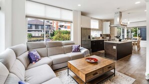 A modern living room with a sofa, coffee table, and kitchen area with a large island. - Perch - Traveler's Gem: Walk to Space Needle | 3BR/3BA Home w Views (Seattle)