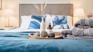 A neatly made bed with a blue and white pillow, a wooden tray with decorative items, and a stack of towels. - Perch - Traveler's Gem: Walk to Space Needle | 3BR/3BA Home w Views (Seattle)