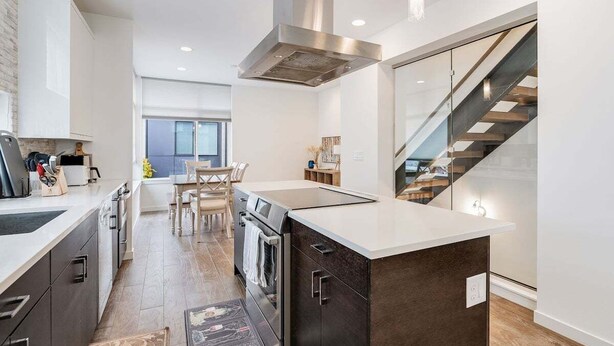 A modern kitchen with a central island, stainless steel range hood, and a staircase leading to an upper level. - Perch - Traveler's Gem: Walk to Space Needle | 3BR/3BA Home w Views (Seattle)