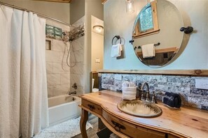 Une salle de bain avec une baignoire, un meuble-lavabo en bois avec un évier, un miroir et un espace douche.