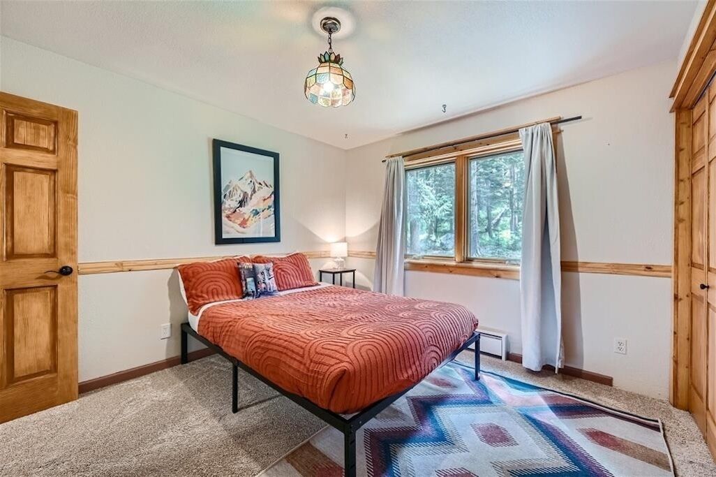 Ein Schlafzimmer mit Bett, einem Fenster mit Vorhängen, einer Holztür und einer an der Wand befestigten Lampe.