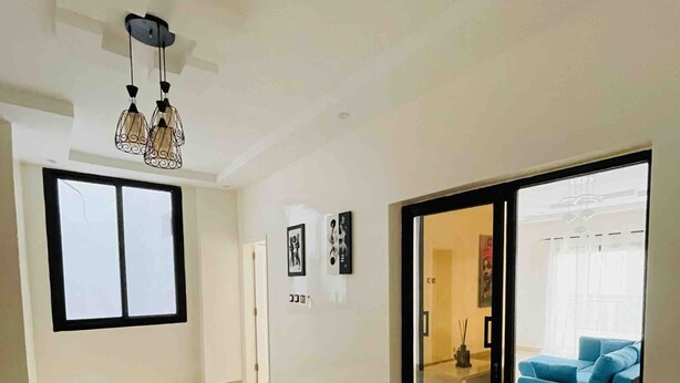 A spacious living area with a large sliding glass door leading to a balcony, a modern chandelier, and a blue sofa. - Chambre privé en résidence sécurisée (Dakar)