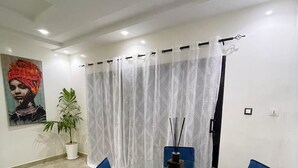 A modern dining area with a glass table and blue chairs, a potted plant, and a painting on the wall. - Chambre privé en résidence sécurisée (Dakar)
