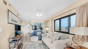 A living room with a white sofa, a coffee table, a TV, and a kitchen in the background.