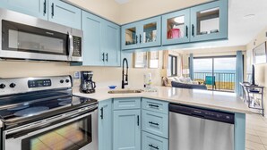 A modern kitchen with stainless steel appliances, light blue cabinetry, and a large window overlooking a balcony.