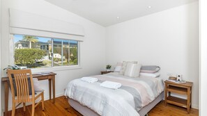Une chambre avec un grand lit, une chaise en bois, un bureau et une fenêtre donnant sur des maisons et de la verdure.