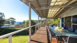 Une terrasse extérieure couverte, dotée d’une table et de chaises, qui offre une vue sur un quartier résidentiel et la mer.