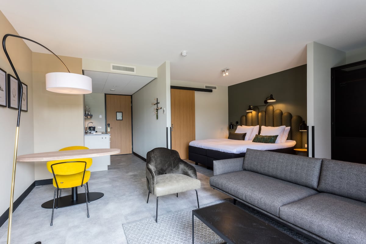 Una camera d'albergo moderna con divano, tavolo da pranzo con sedie, una poltrona, un letto e una scrivania.