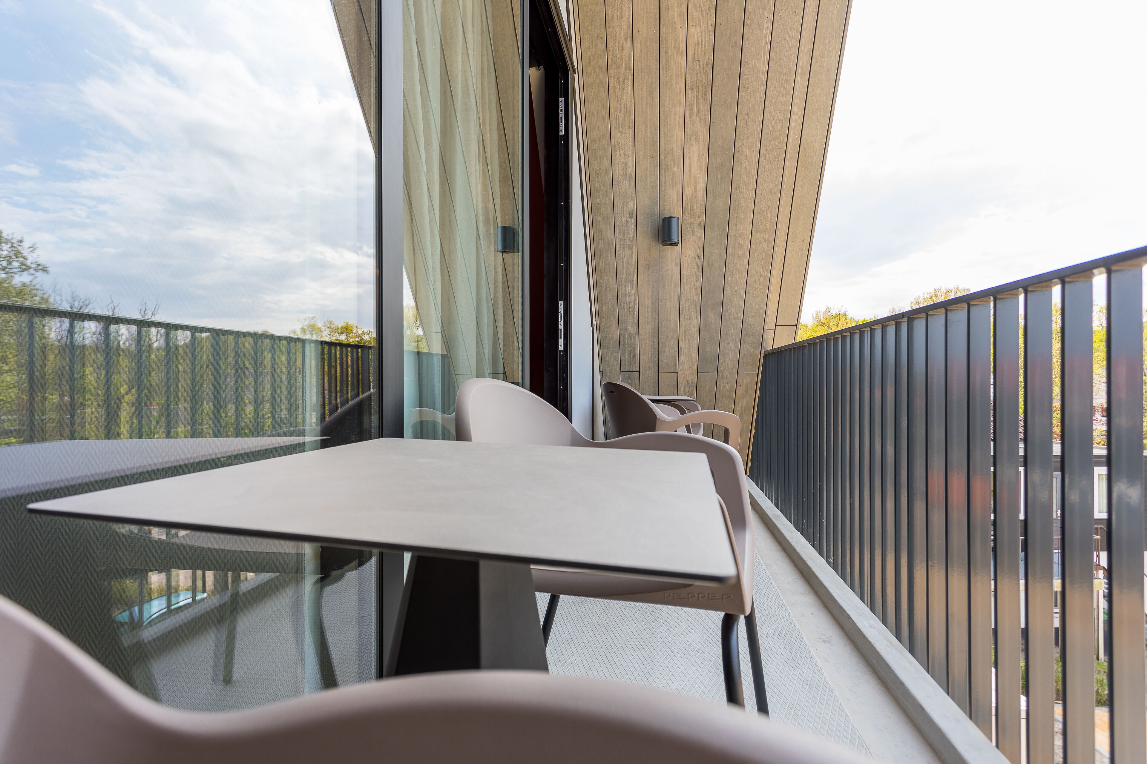 Un balcon moderne avec une table et des chaises en verre, un lambris en bois et une vue sur les arbres.