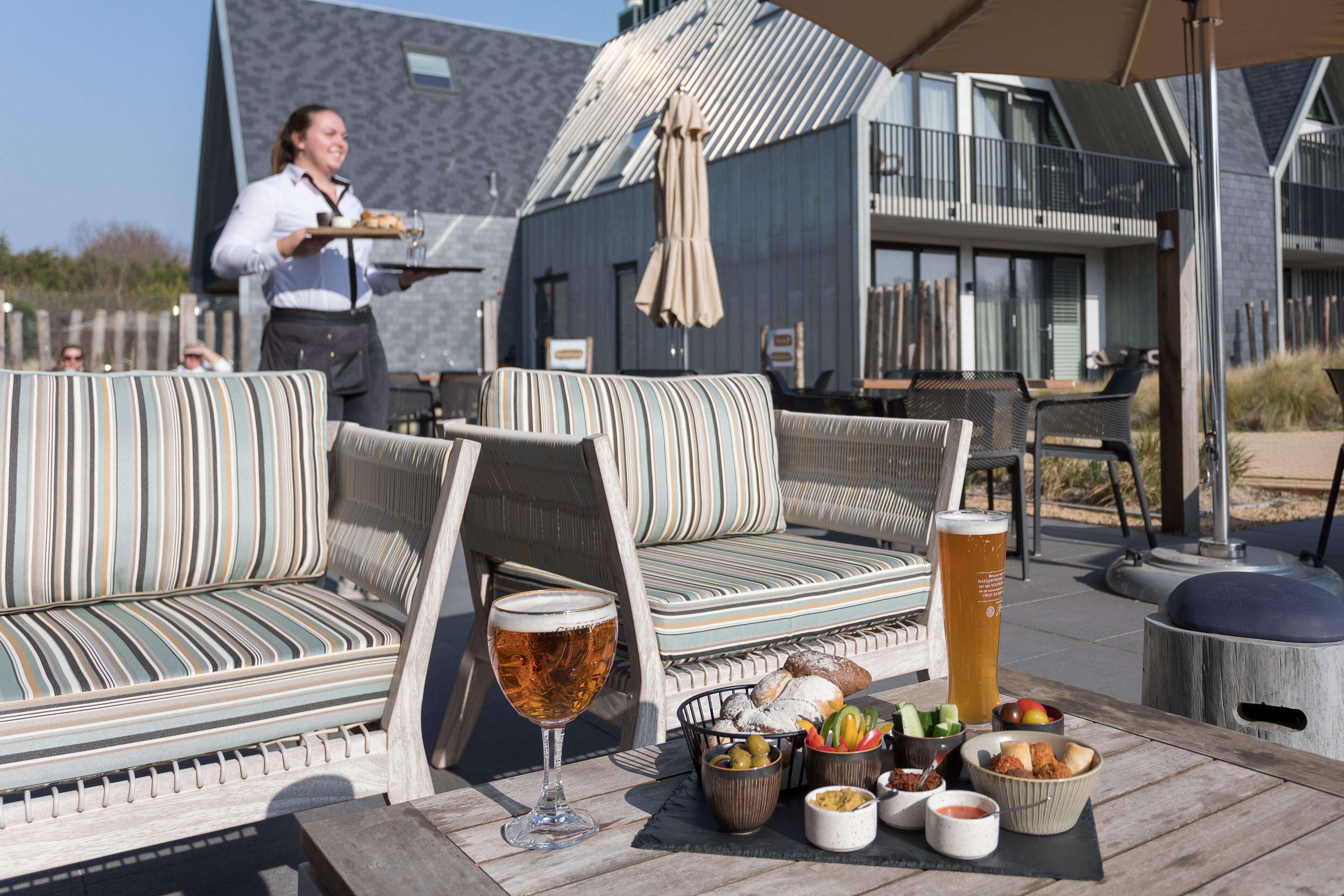 Ein gemütlicher Sitzbereich im Freien mit gestreiften Kissen, einem Glas Bier und verschiedenen Snacks.