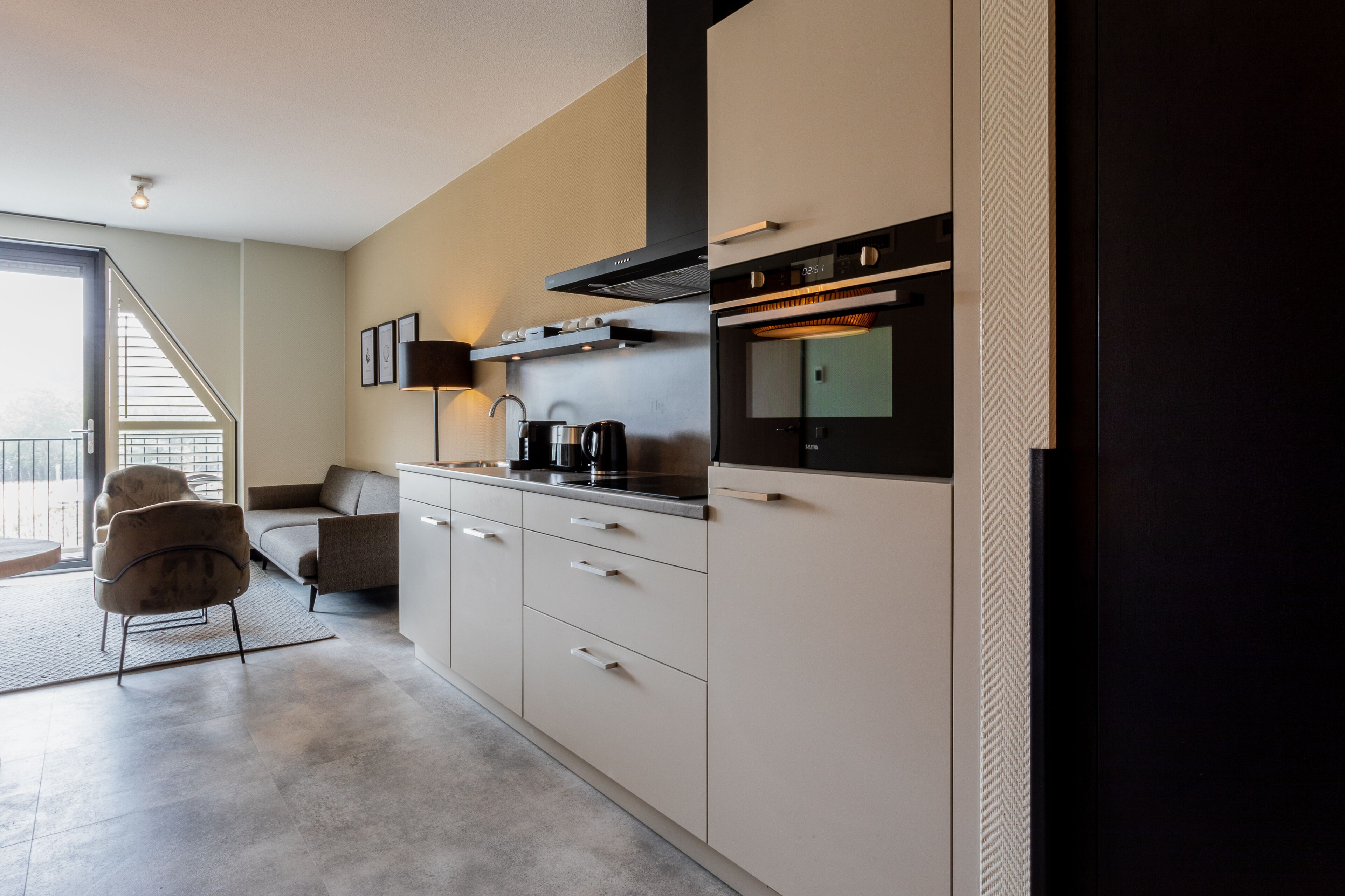 Een moderne keuken met een inbouwoven, een koffiezetapparaat en een bank in de aangrenzende woonkamer.