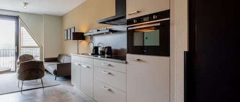 Een moderne keuken met een inbouwoven, een koffiezetapparaat en een bank in de aangrenzende woonkamer.