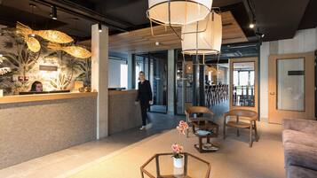 A modern reception area with a wooden reception desk, a seating area with a sofa and chairs, and a decorative plant centerpiece.