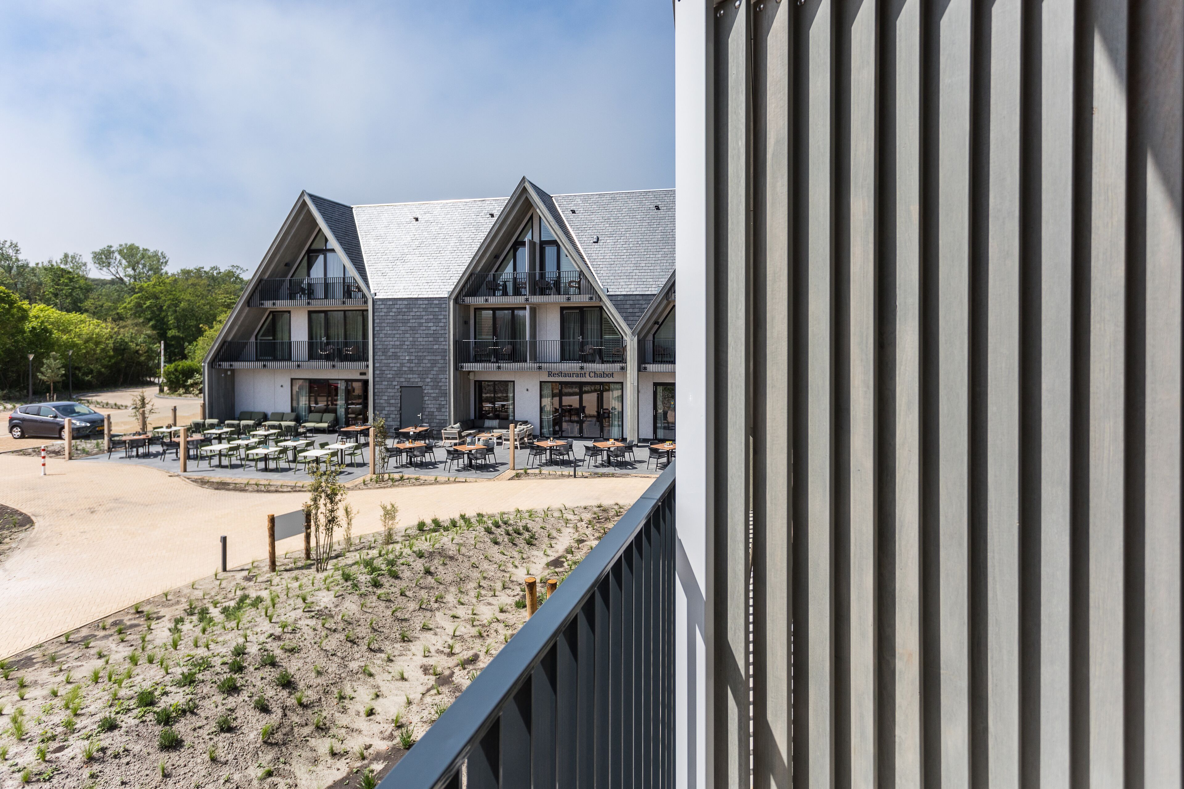 Een modern gebouw met op de begane grond 'Restaurant Chalet', met terras en zitplaatsen.