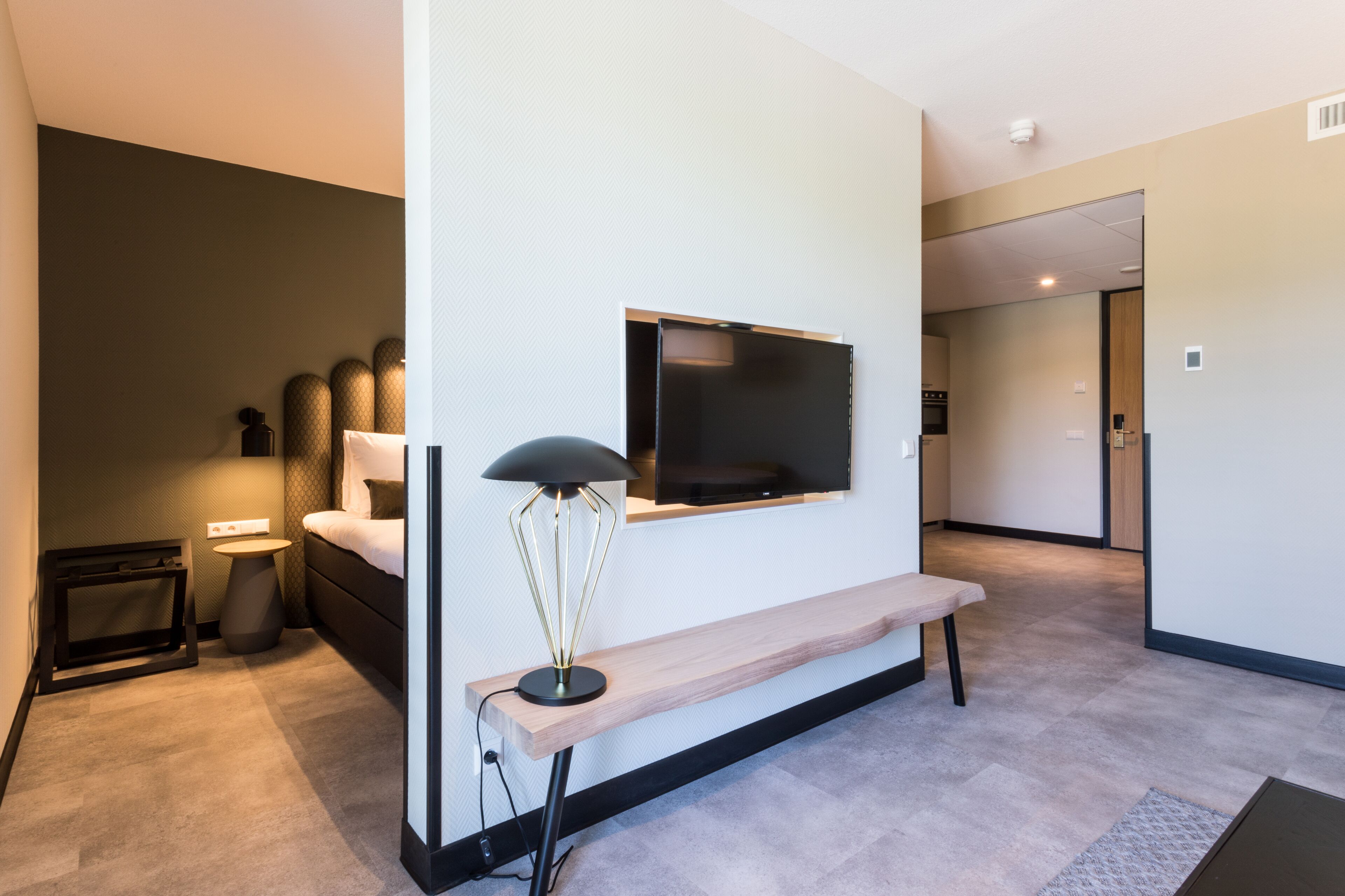 Una habitación de hotel moderna con una cama, mesita de noche, lámpara y televisor montado.