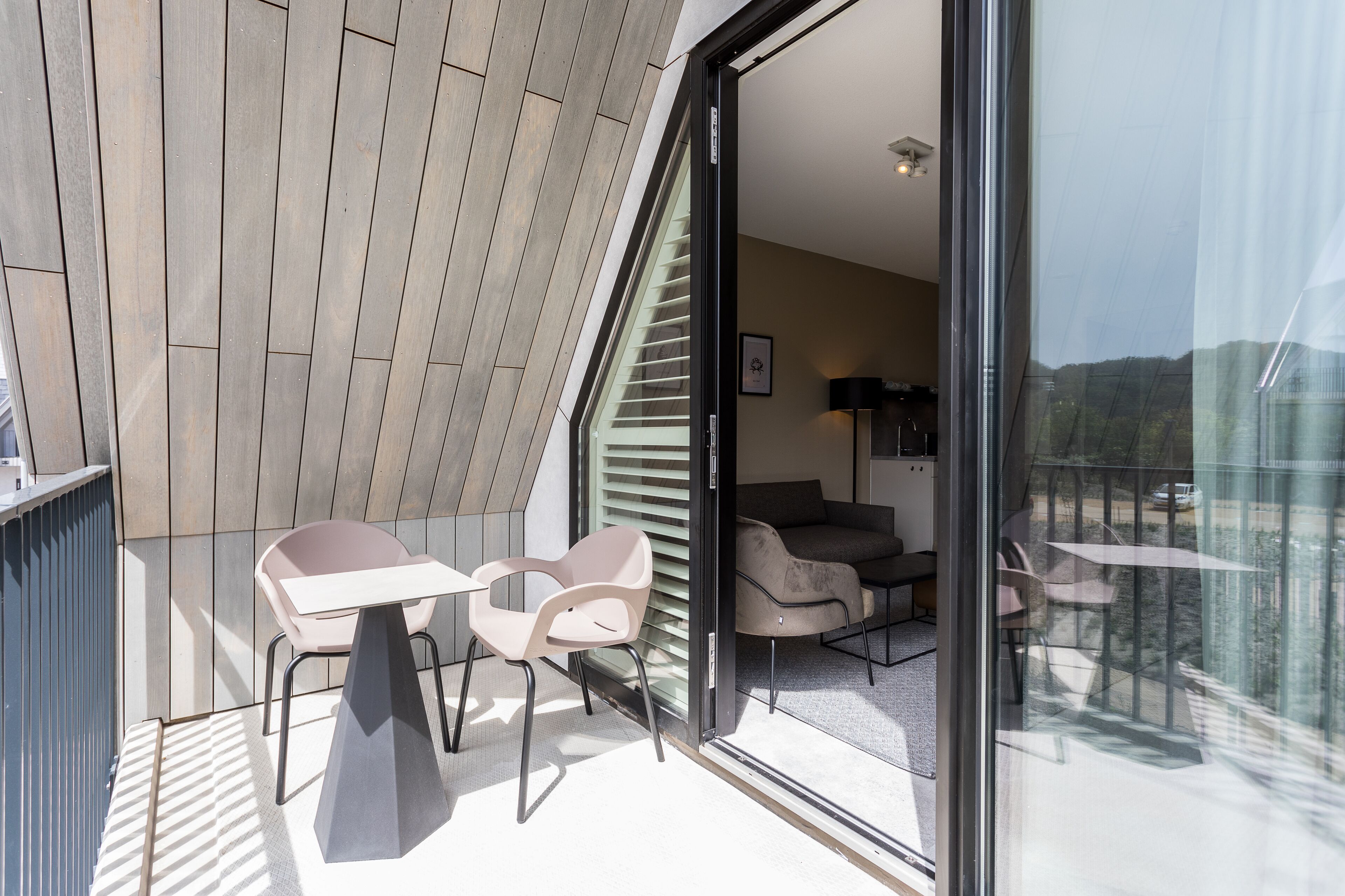 Un balcón moderno con puerta de vidrio que da a una sala de estar con sofá y sillones.